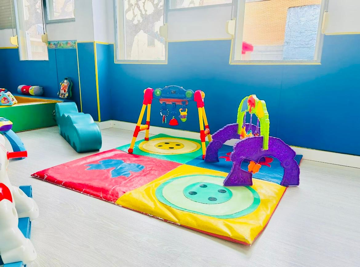 Sala de bebés con alfombra de colores, gimnasios de actividades y juguetes